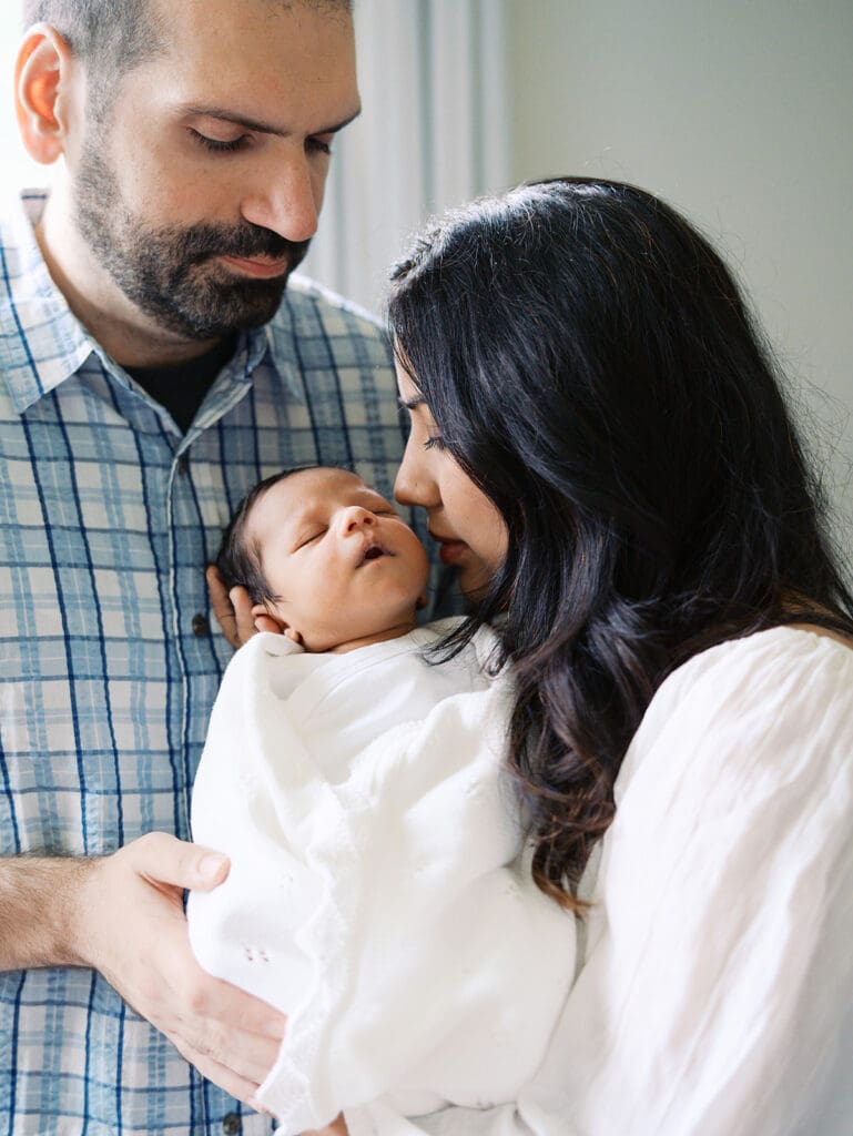 A mom kissing her baby as dad looks at them during a session by Katie Stansfield Photography, a Chesterfield Newborn Photographer.